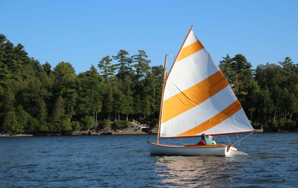 09112026-Sailing_KJLN.006 lowres A sailboat with an orange and white sail in front of trees and a blue sky