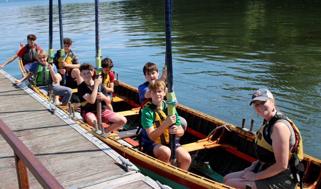 A group of students in a rowing gig holding their oars vertically in the air.