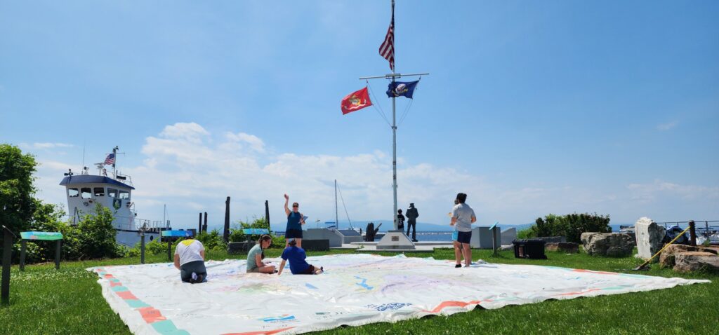 A giant map spread out on a lawn under a blue sky